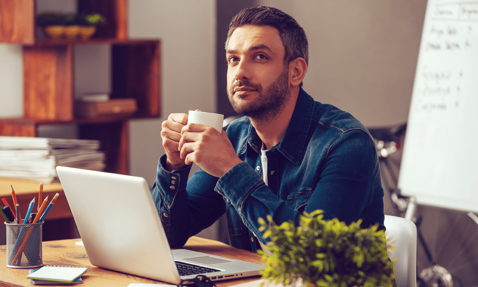 man holding coffee cup at desk looking up and thinking